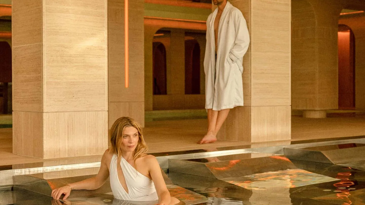 Piscina de spa bajo arcos de piedra en SHA Wellness Clinic en España, una huésped en el agua y otro en albornoz
