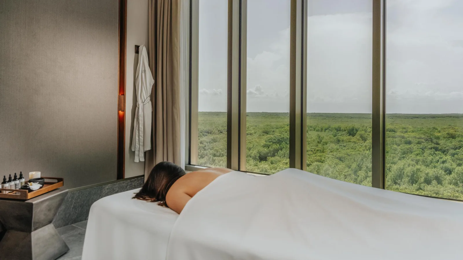 Sala de tratamiento de SHA Wellness Clinic en México, una huésped en la camilla y una ventana al paisaje verde