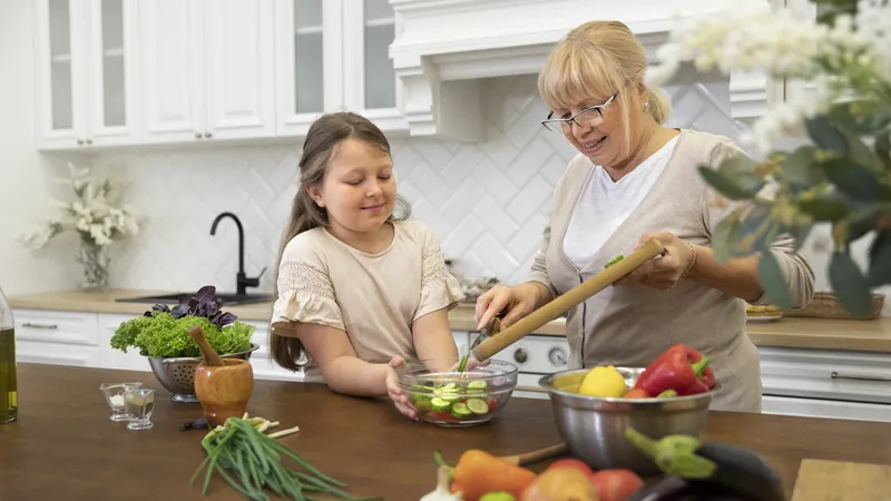 Mujer mayor y niña preparan juntas una ensaladera en la encimera de la cocina