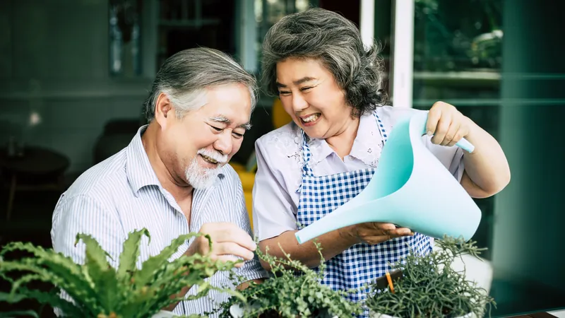 Pareja mayor regando juntos plantas en maceta con una regadera